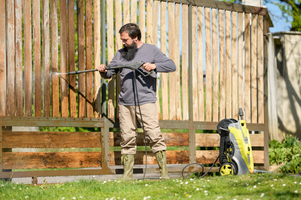 Mid adult man cleaning a wooden gate with a power washer