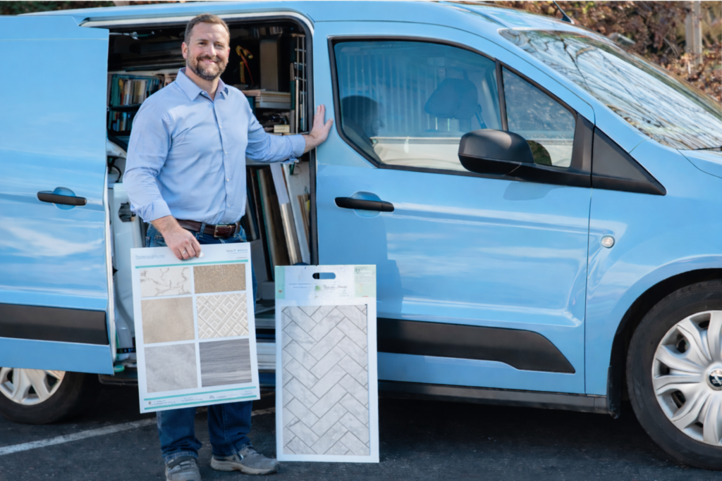 Mobile flooring franchise with the Design Associate holding sample tiles at the open door of a sky-blue van