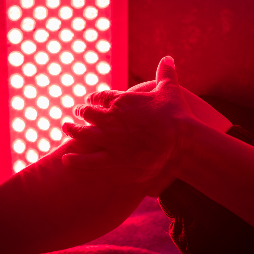 Hands positioned in front of a red light therapy panel inside a modern preventive health and longevity wellness center